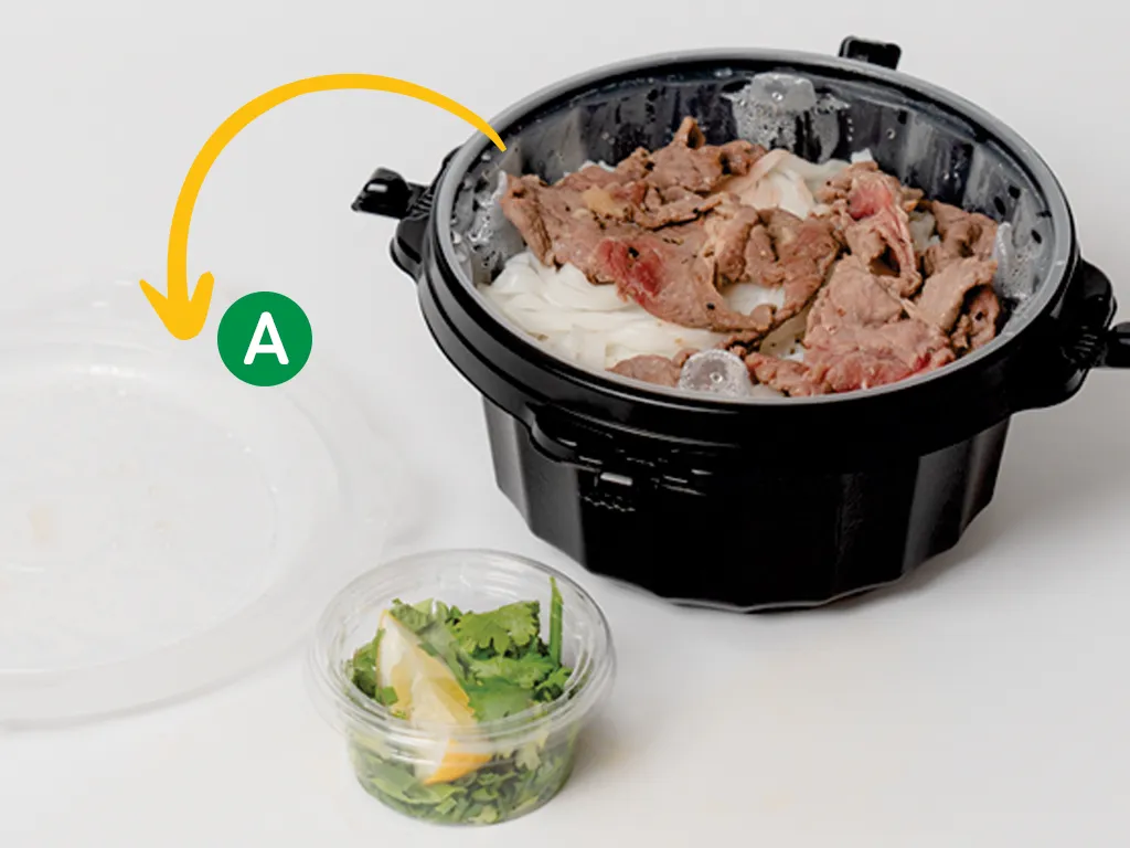 外蓋（A）を外して裏返す様子。奥に麺と肉の入った容器、手前に薬味のカップ。
